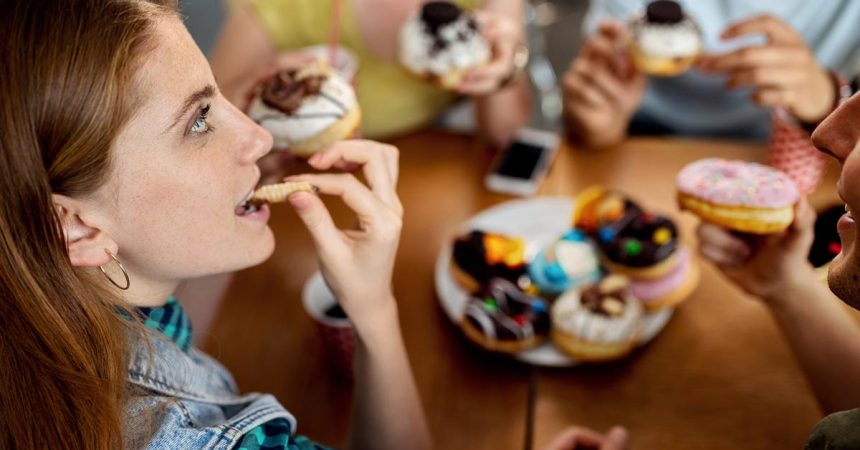 Young woman and her friends eating glazed donuts in a cafe.